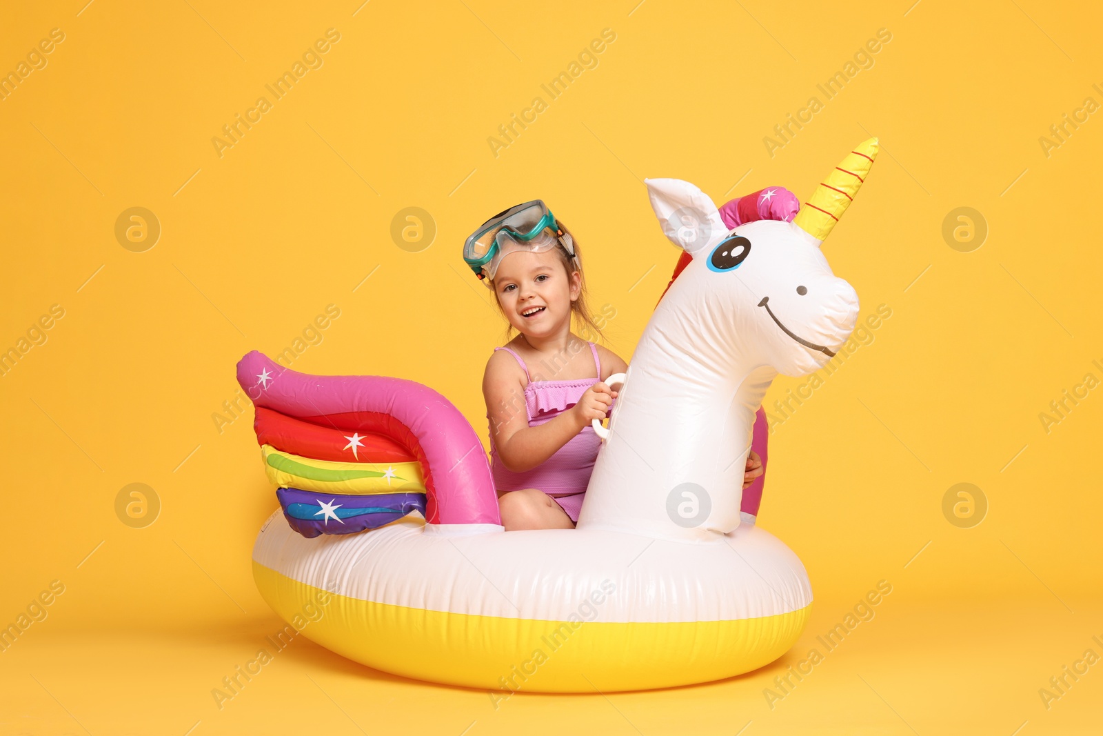 Photo of Cute little girl in swimsuit with unicorn pool float on orange background