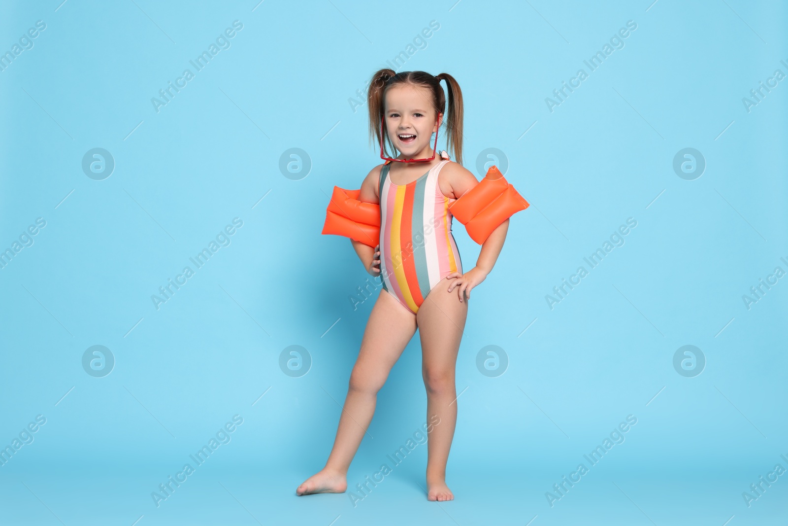 Photo of Cute little girl in swimsuit with swim armbands on light blue background