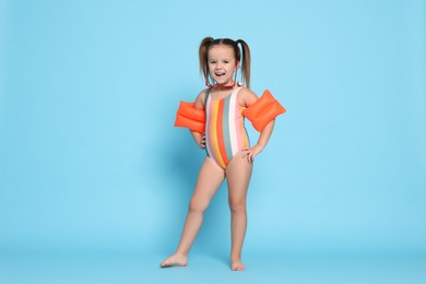 Photo of Cute little girl in swimsuit with swim armbands on light blue background