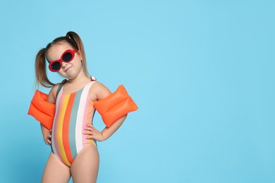 Cute little girl in swimsuit with swim armbands on light blue background. Space for text