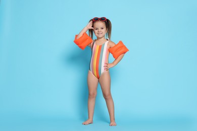 Photo of Cute little girl in swimsuit with swim armbands on light blue background