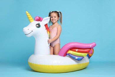 Cute little girl in swimsuit with unicorn pool float on light blue background