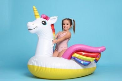 Photo of Cute little girl in swimsuit with unicorn pool float on light blue background