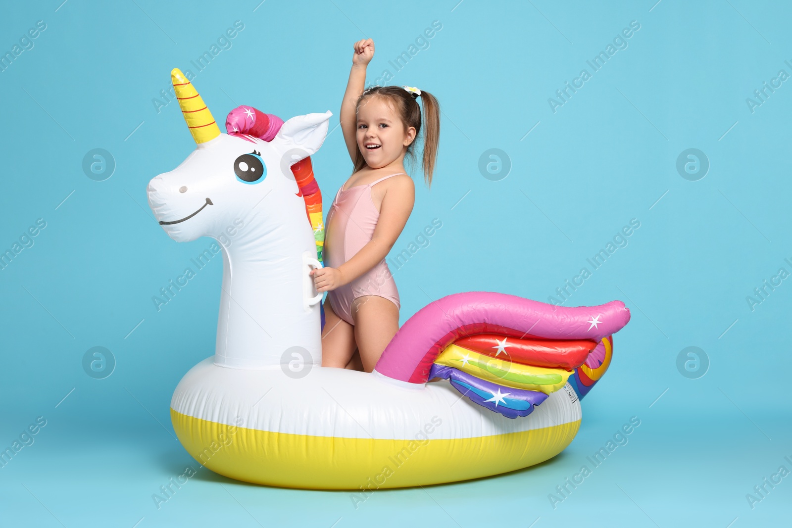 Photo of Cute little girl in swimsuit with unicorn pool float on light blue background