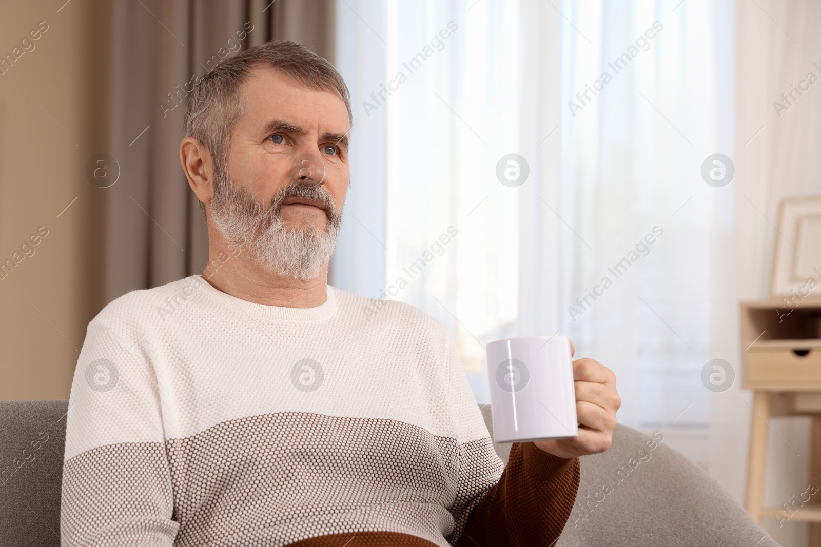 Photo of Mature man with cup of hot drink on sofa at home. Space for text