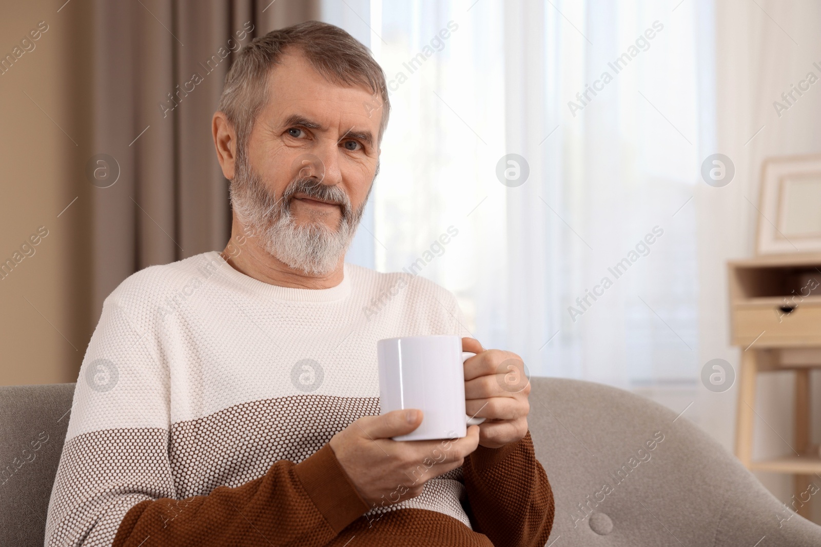 Photo of Mature man with cup of hot drink on sofa at home