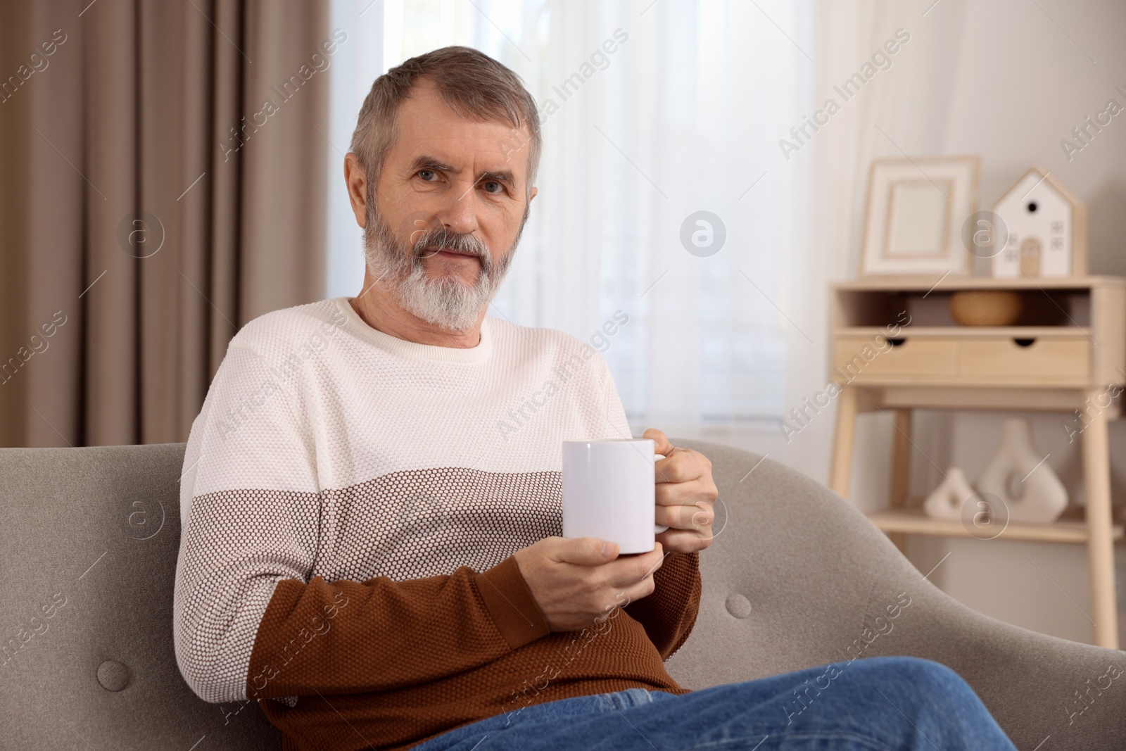 Photo of Mature man with cup of hot drink on sofa at home