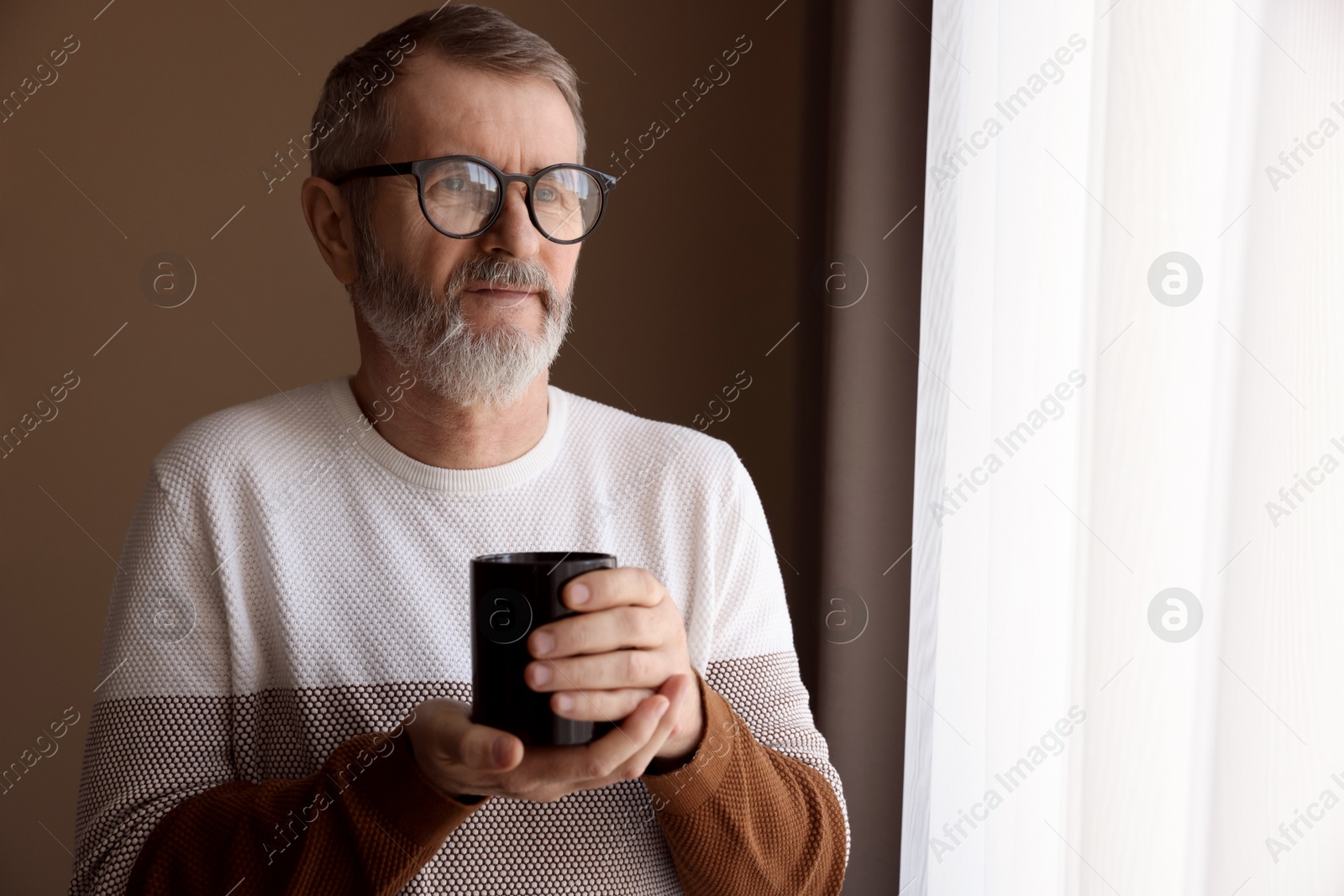 Photo of Mature man with cup of hot drink at home. Space for text