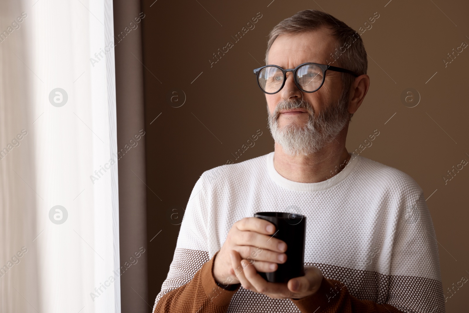 Photo of Mature man with cup of hot drink at home. Space for text