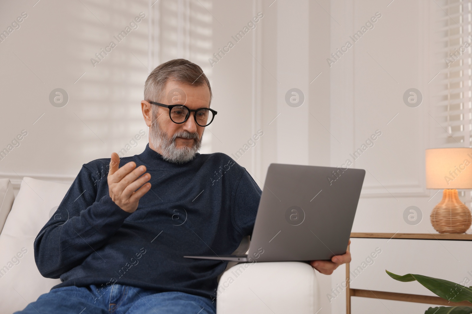 Photo of Mature man having videochat by laptop on sofa at home