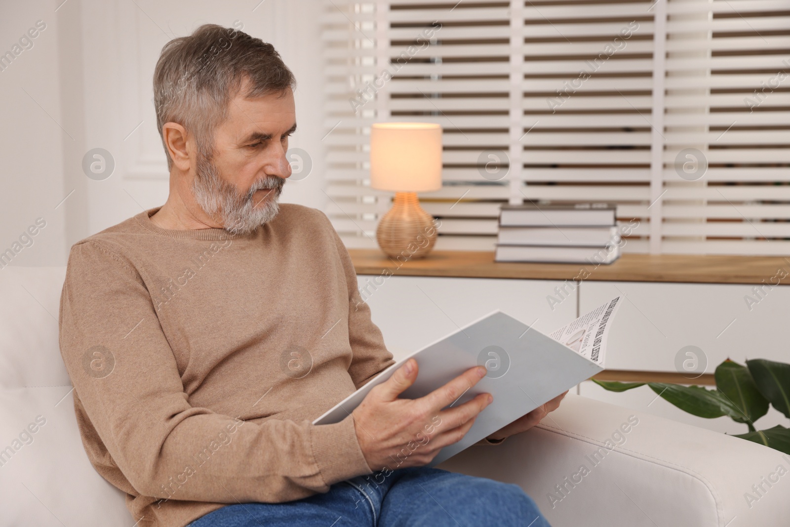 Photo of Mature man reading magazine on sofa at home