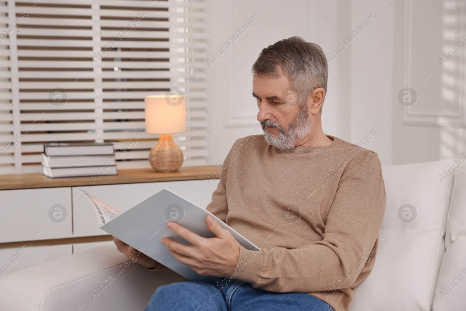 Photo of Mature man reading magazine on sofa at home