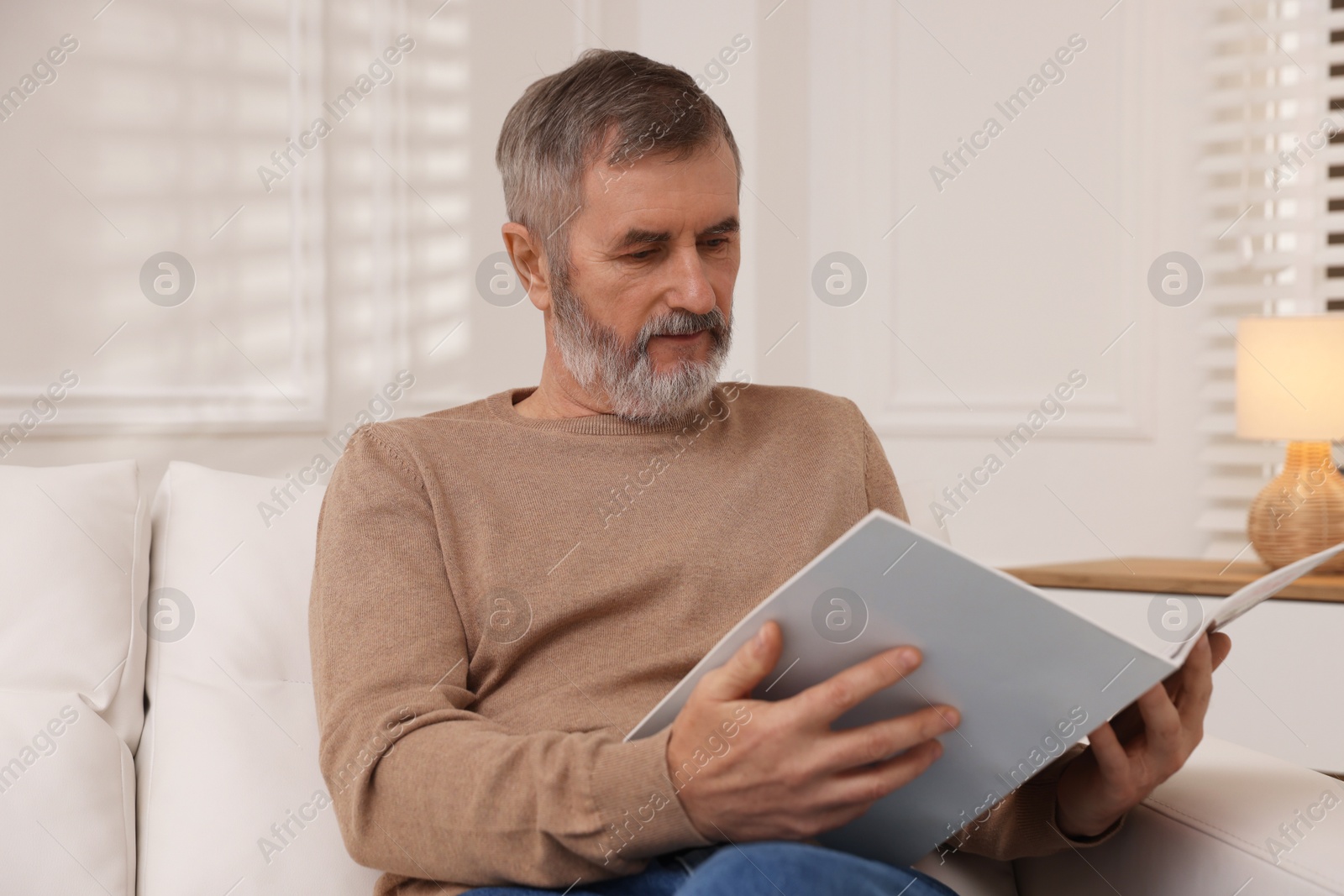 Photo of Mature man reading magazine on sofa at home