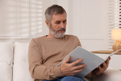 Mature man reading magazine on sofa at home