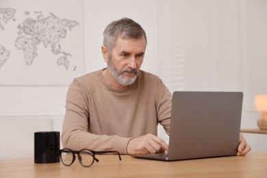 Photo of Mature man with laptop at table indoors