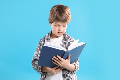 Photo of Learning alphabet. Little boy with book on light blue background