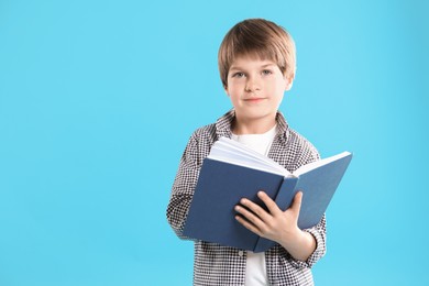 Photo of Learning alphabet. Little boy with book on light blue background, space for text