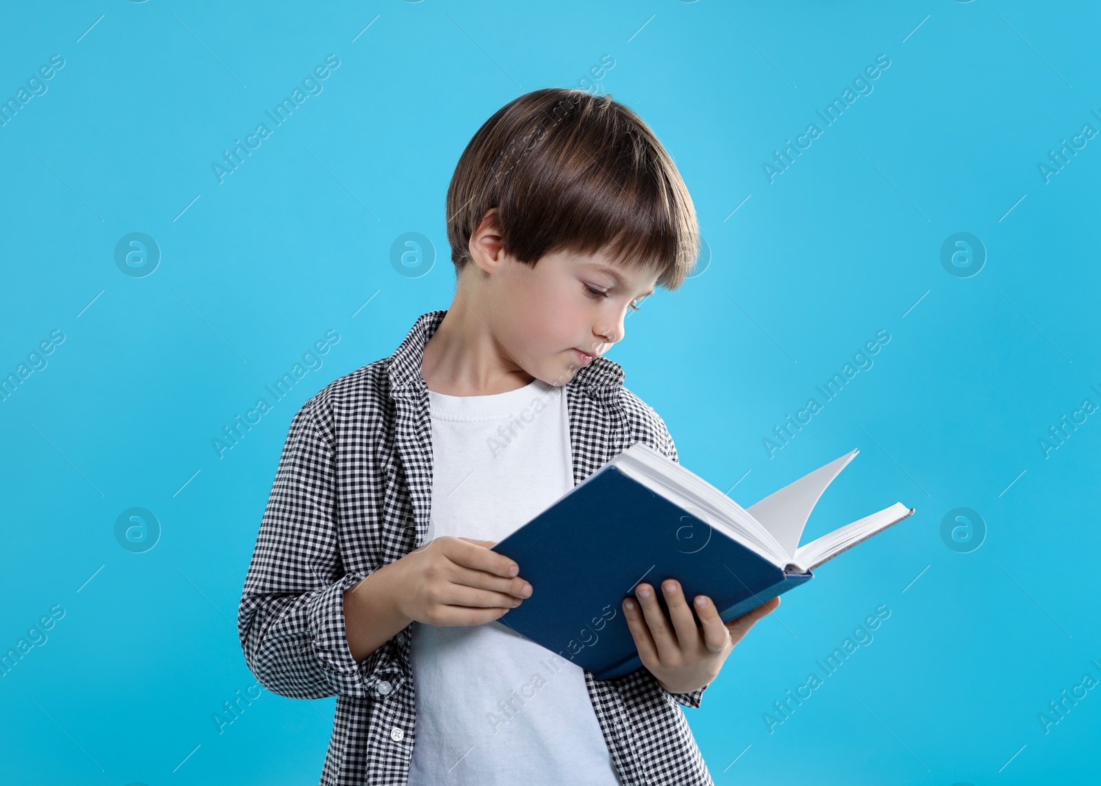 Photo of Learning alphabet. Little boy with book on light blue background