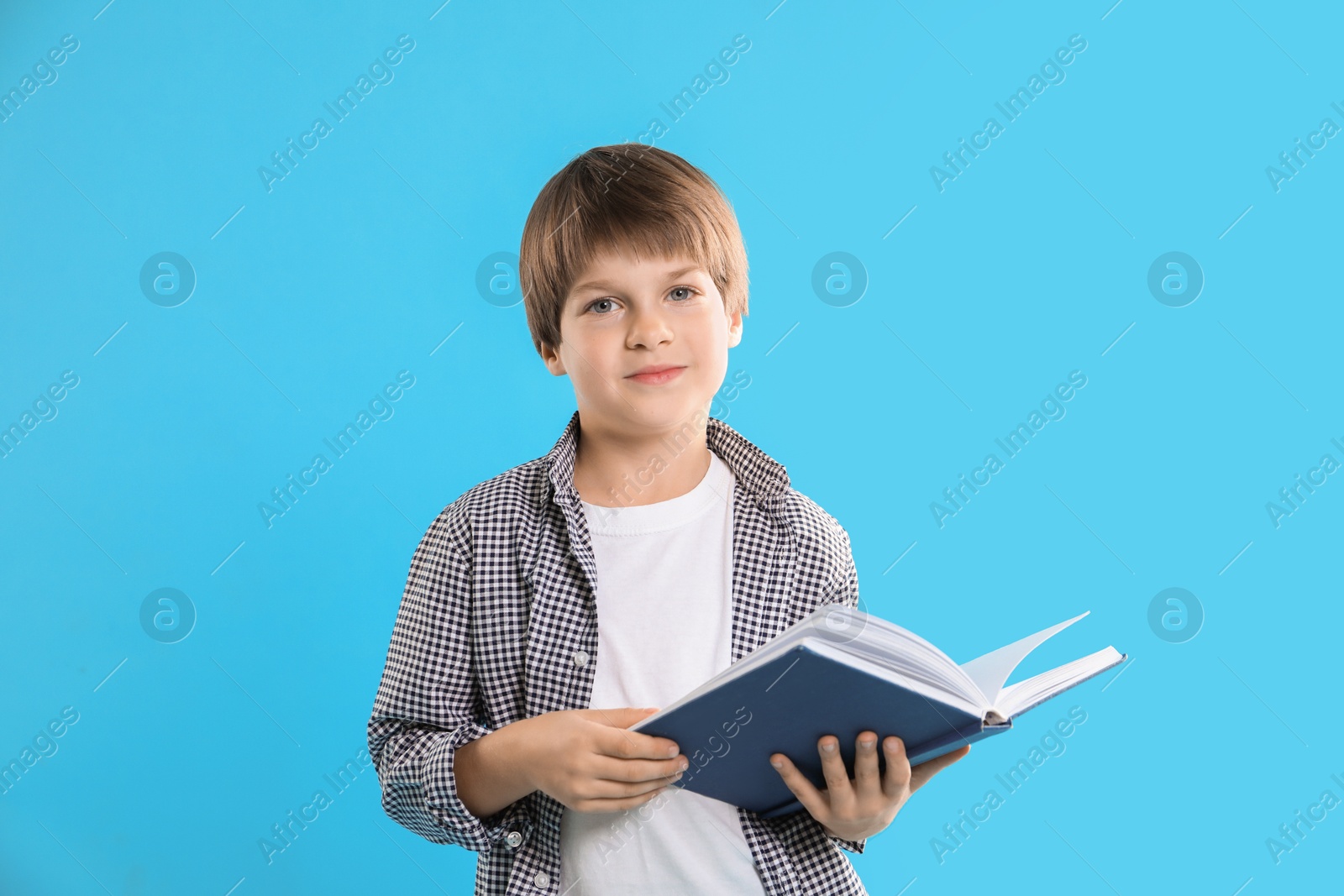 Photo of Learning alphabet. Little boy with book on light blue background