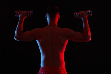 Photo of Man exercising with dumbbells in red light on black background, back view