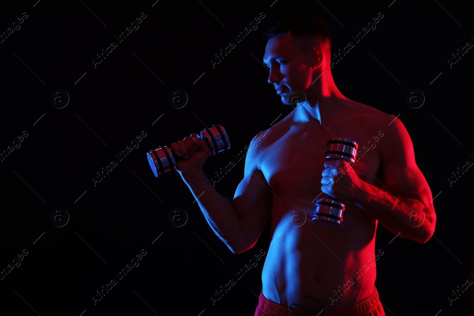 Photo of Man exercising with dumbbells in red light on black background. Space for text