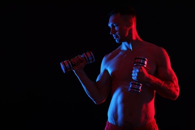 Photo of Man exercising with dumbbells in red light on black background. Space for text