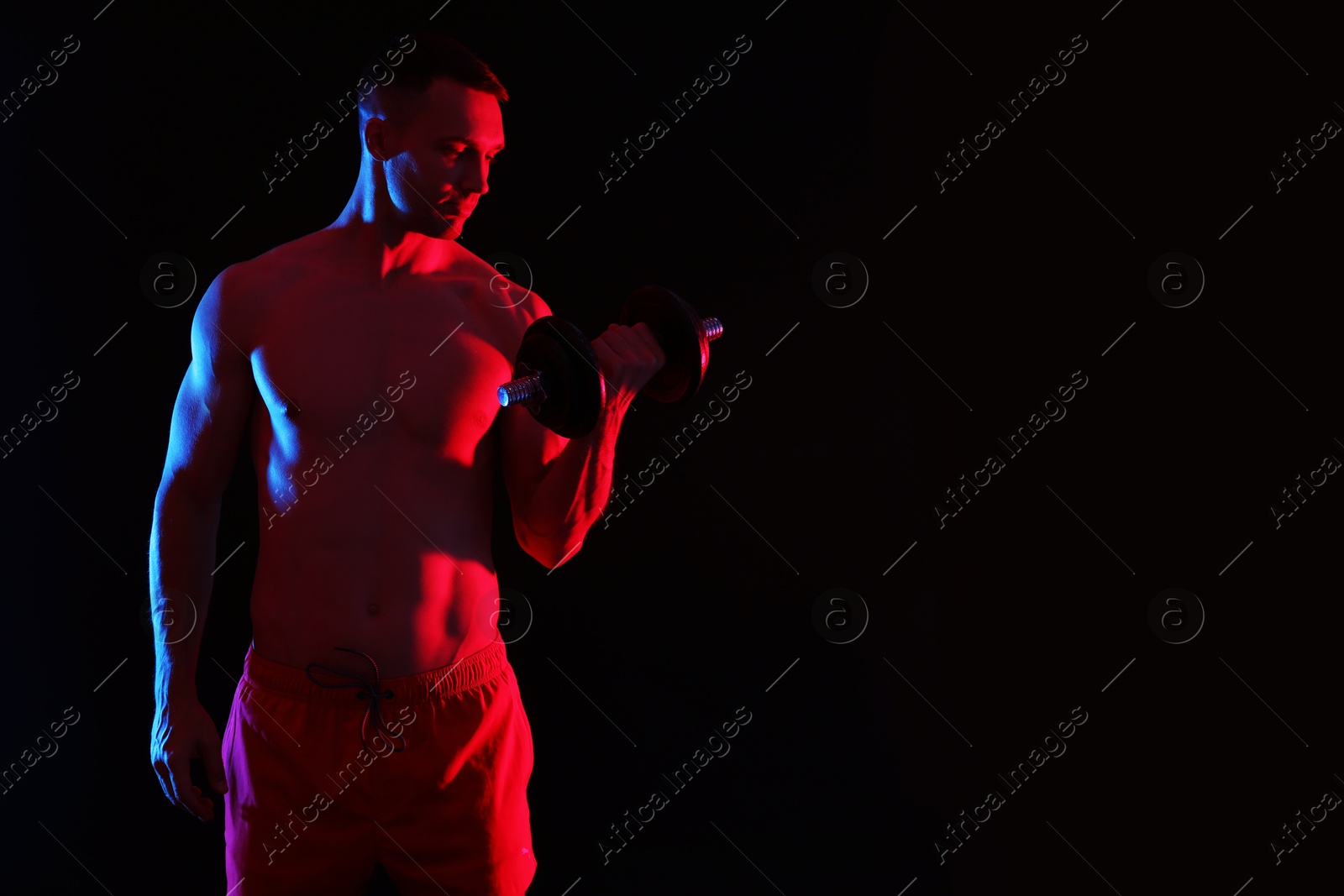 Photo of Man exercising with dumbbell in red light on black background, space for text