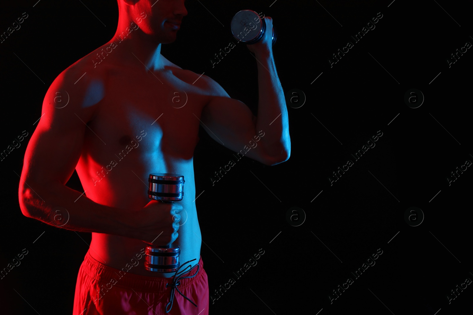 Photo of Man exercising with dumbbells in red light on black background, closeup. Space for text