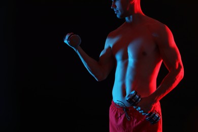 Photo of Man exercising with dumbbells in red light on black background, closeup. Space for text