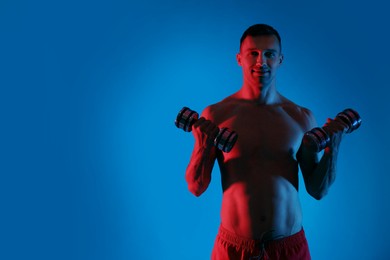 Photo of Man exercising with dumbbells in red light on blue background, space for text