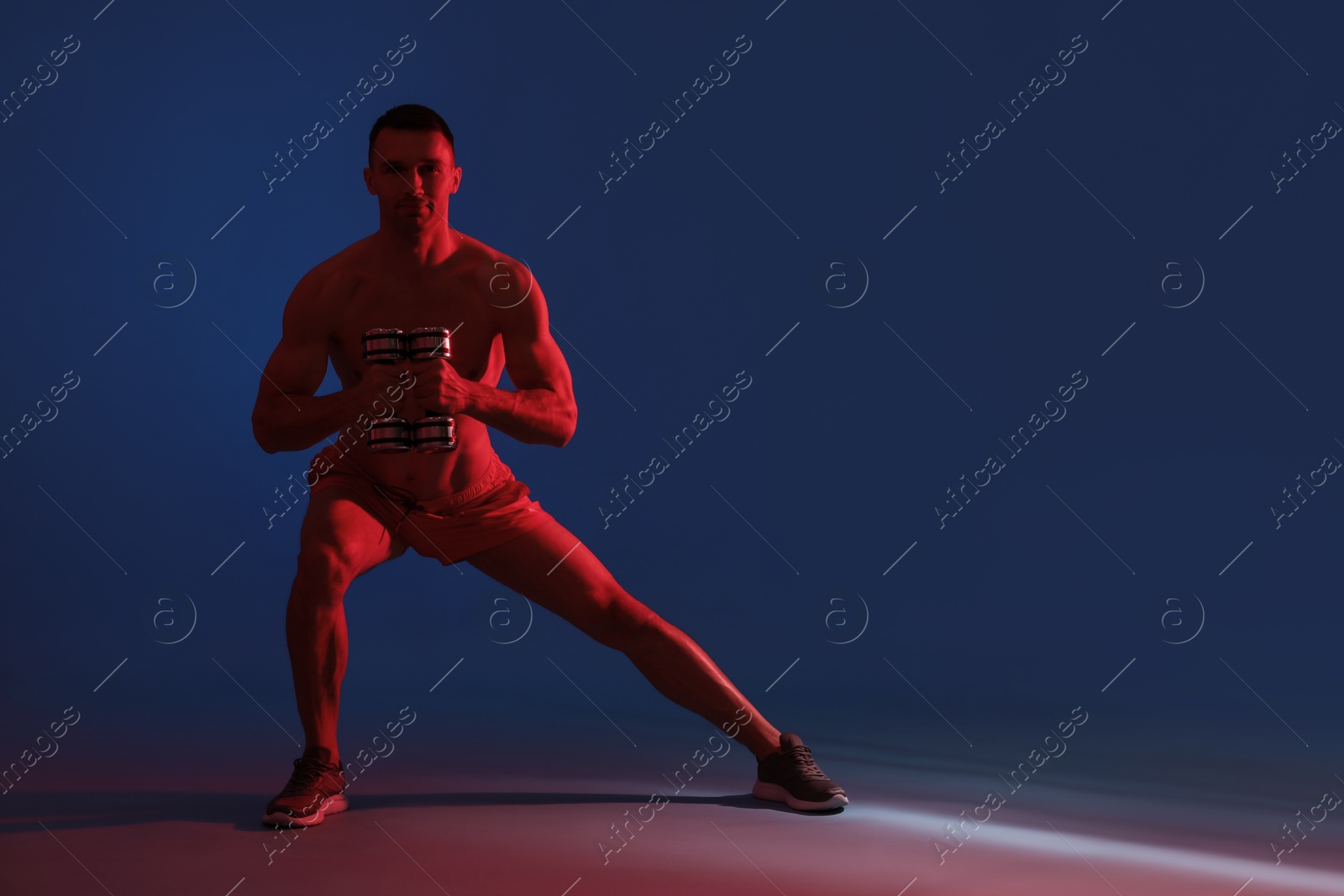 Photo of Man exercising with dumbbells in red light on blue background, space for text