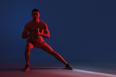 Photo of Man exercising with dumbbells in red light on blue background, space for text