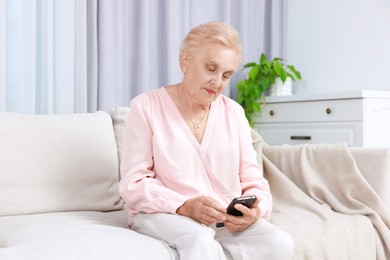 Photo of Senior woman using smartphone on sofa at home