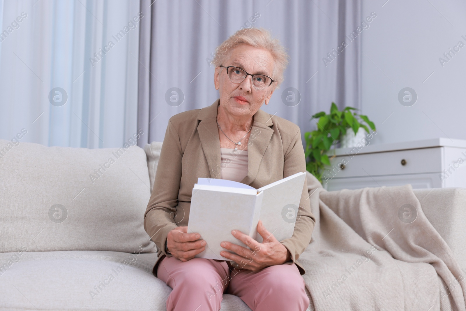 Photo of Senior woman reading book on sofa at home