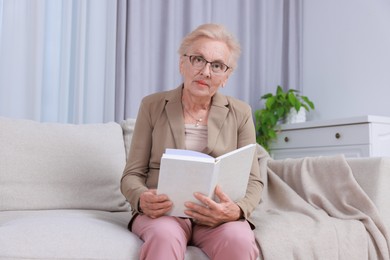 Photo of Senior woman reading book on sofa at home