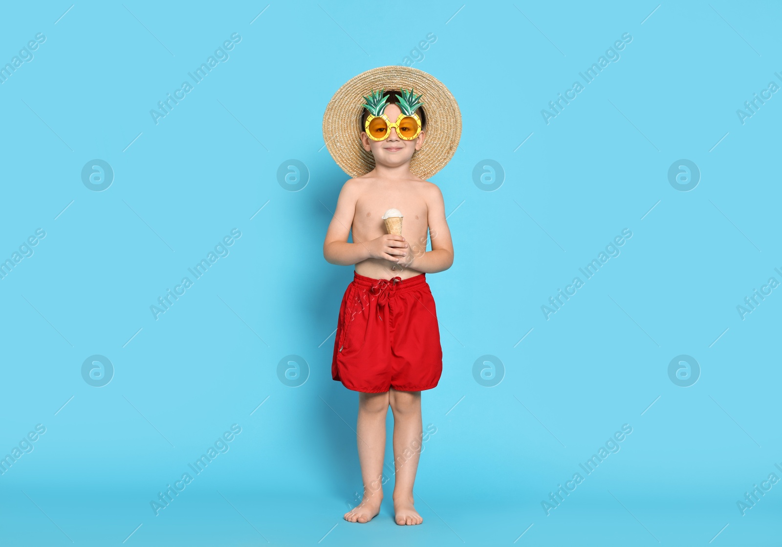 Photo of Cute little boy in beachwear with ice cream on light blue background