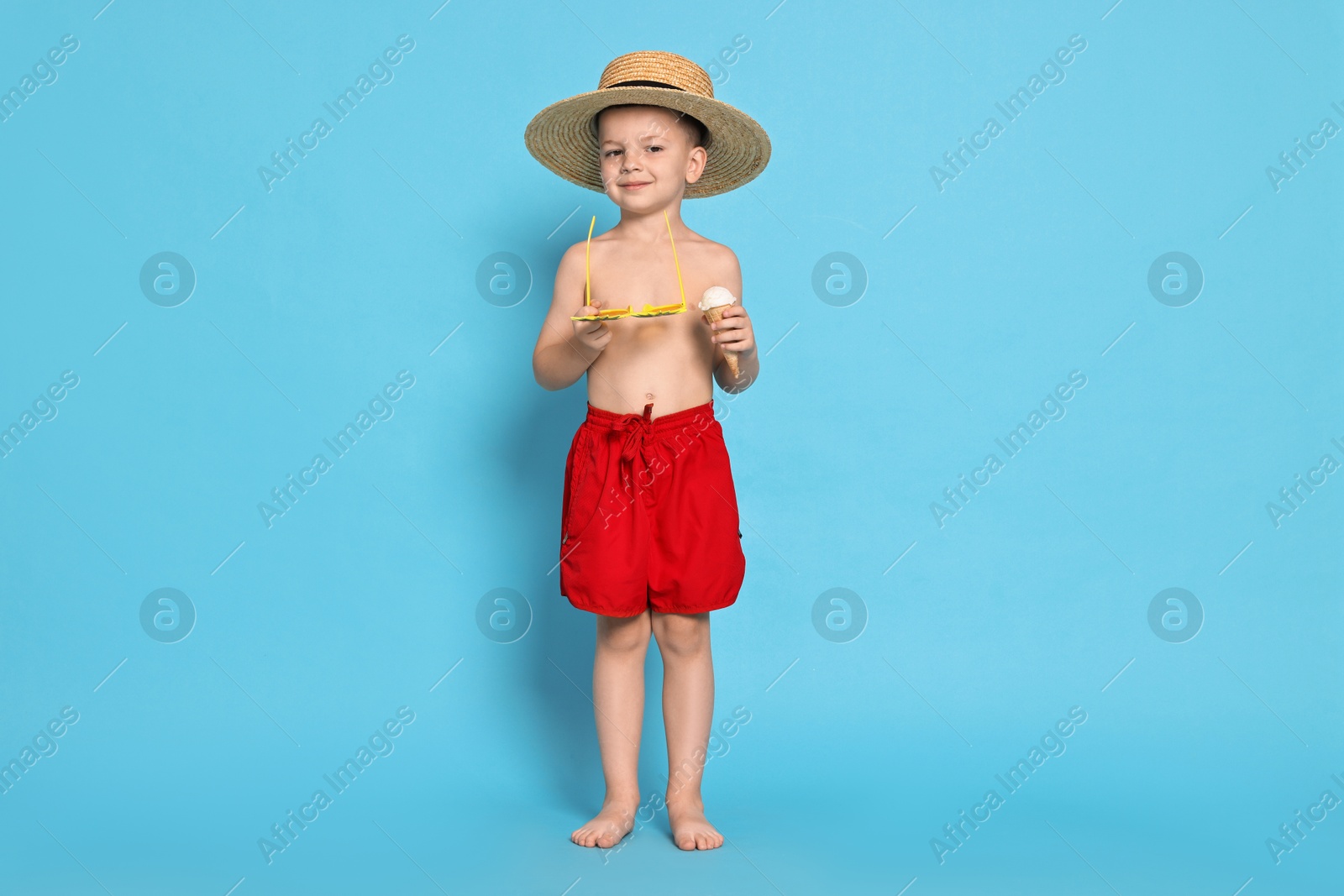 Photo of Cute little boy in beachwear with ice cream on light blue background