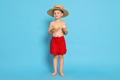 Cute little boy in beachwear with ice cream on light blue background