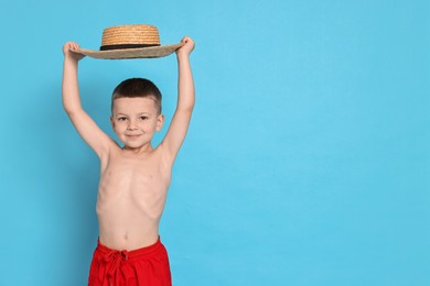 Photo of Cute little boy in beachwear with straw hat on light blue background. Space for text