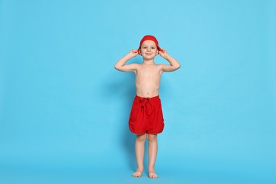 Photo of Cute little boy in beachwear with swim cap on light blue background