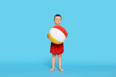 Photo of Cute little boy in beachwear with inflatable ball on light blue background