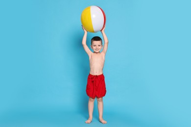 Photo of Cute little boy in beachwear with inflatable ball on light blue background