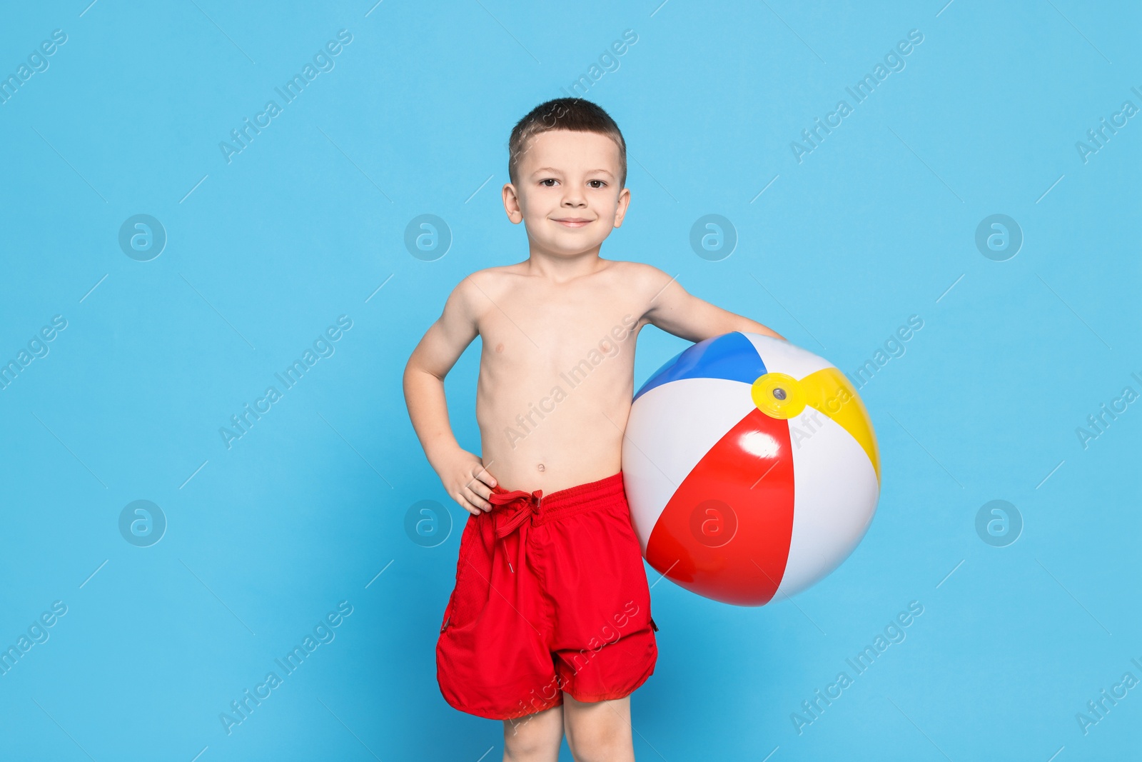 Photo of Cute little boy in beachwear with inflatable ball on light blue background