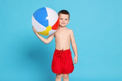 Photo of Cute little boy in beachwear with inflatable ball on light blue background