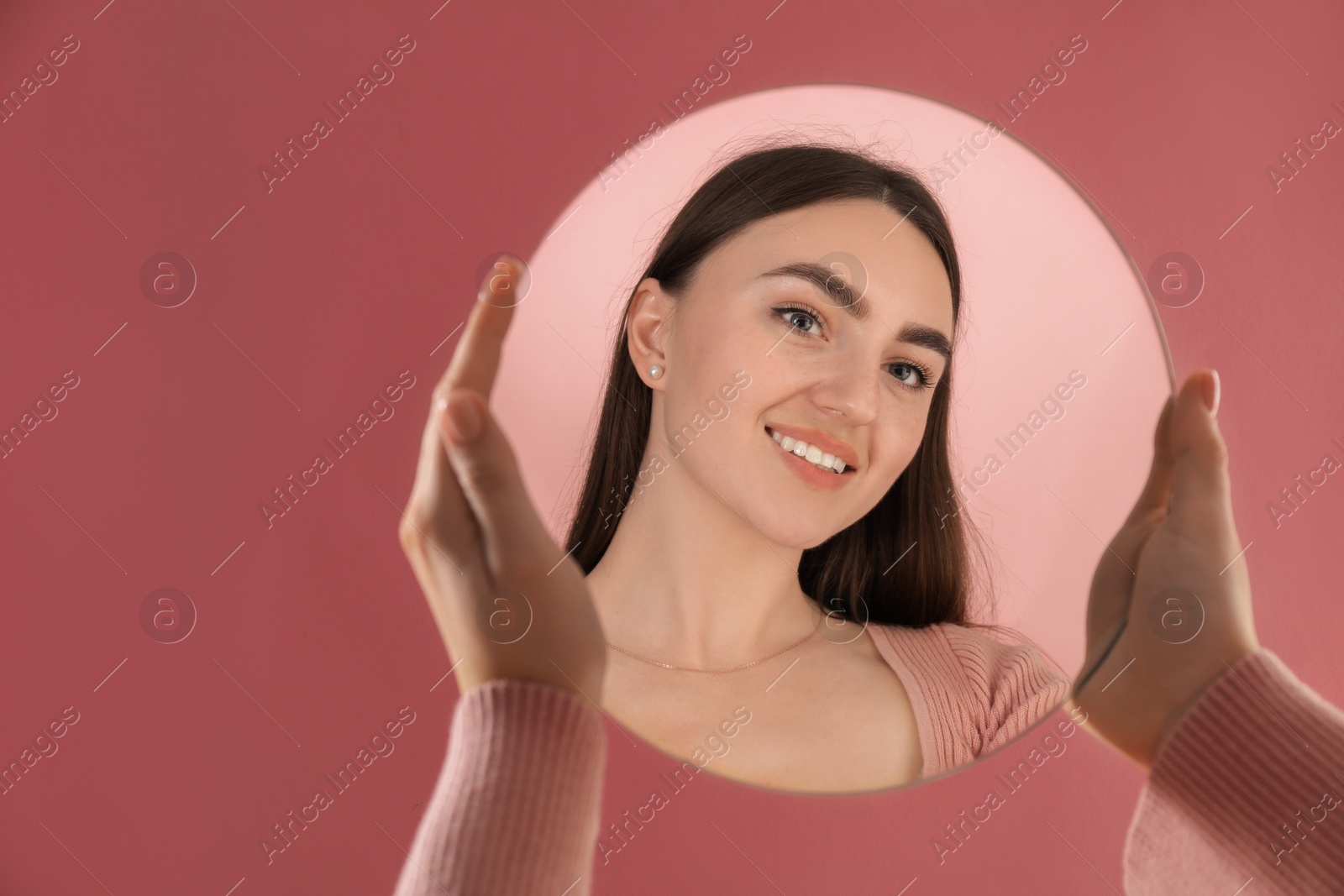 Photo of Woman holding round mirror on pink background, closeup. Space for text