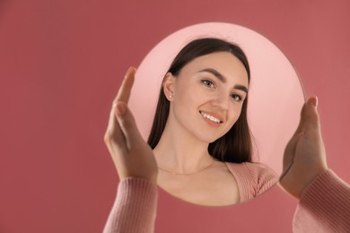 Woman holding round mirror on pink background, closeup. Space for text