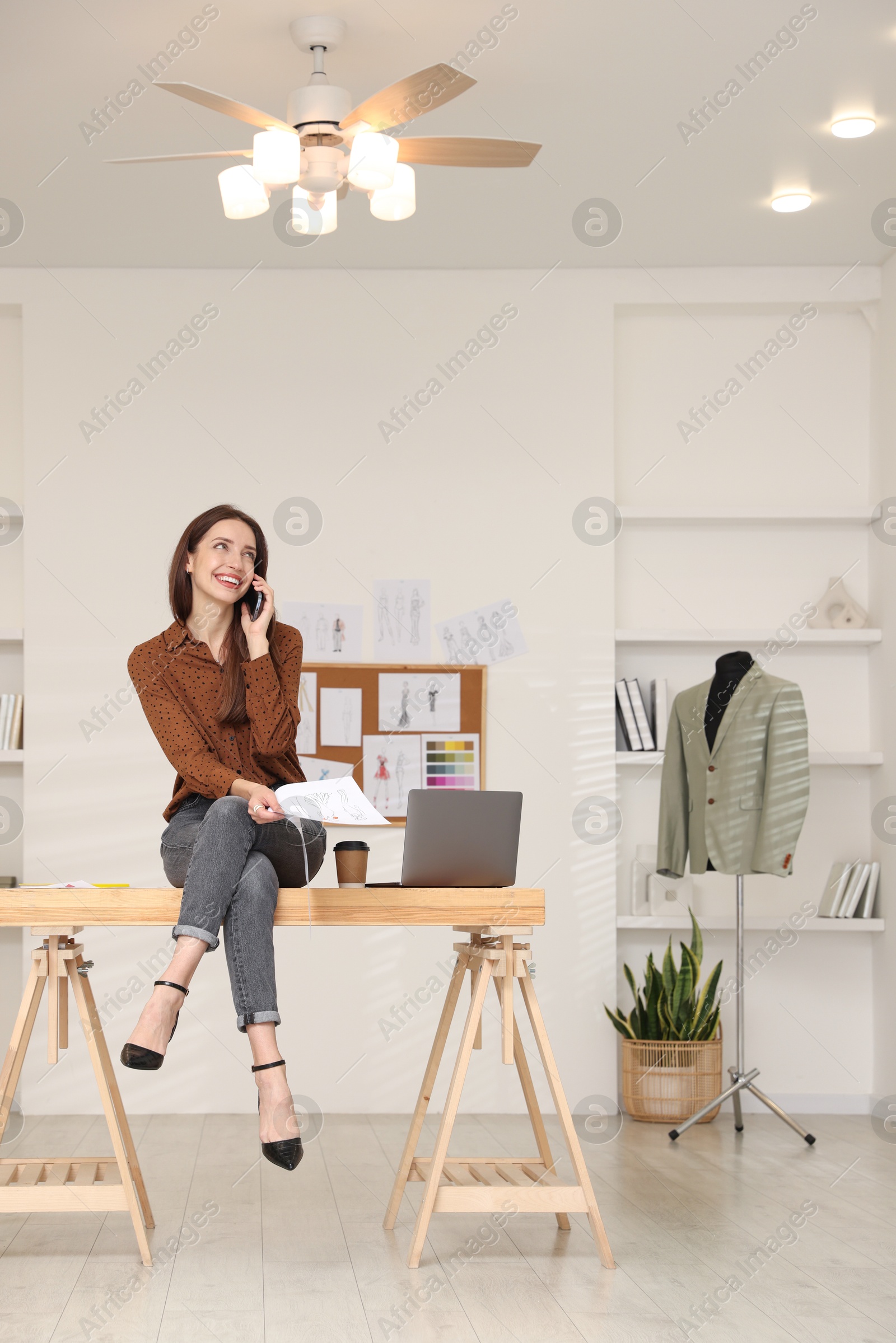 Photo of Fashion designer talking on smartphone in workshop