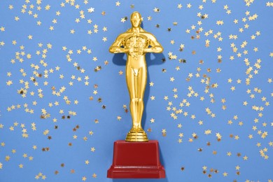 Photo of Golden trophy in shape of human figure and shiny confetti on light blue background, top view