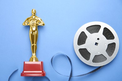 Photo of Golden trophy in shape of human figure and film reel on light blue background, top view