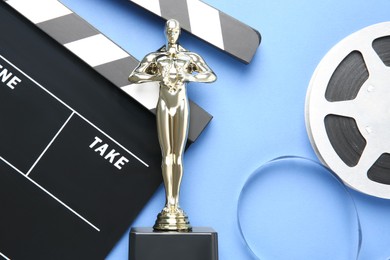 Photo of Golden trophy in shape of human figure, movie clapper and film reel on light blue background, top view